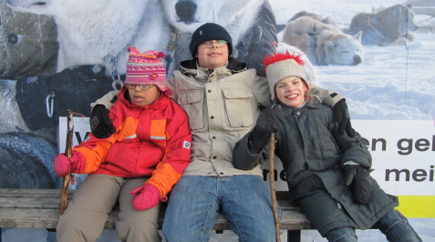 Drei Kinder mit Handicaps sitzen mit Muetzen und warm gekleidet im Winter auf einer Bank