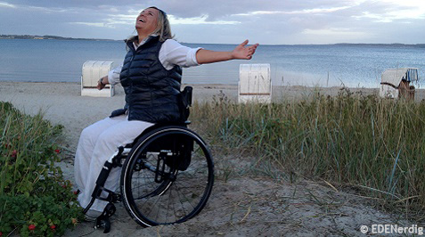 Rollstuhlfahrerin am Strand mit ausgebreiteten Armen