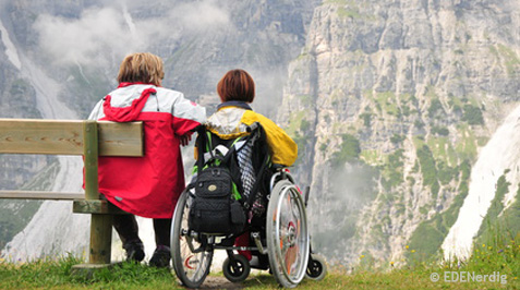 Rollstuhlfahrerin und Fußgängerin schauen auf ein Bergpanorama