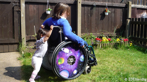 Ein kleines Kind schiebt eine Frau im Rollstuhl über eine Wiese