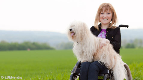Junge Frau im Rollstuhl mit Hund auf dem Schoss