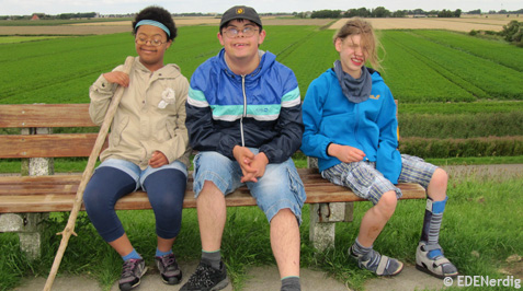 Drei Kinder mit Handicaps machen auf einer Bank Pause bei einer Wanderung